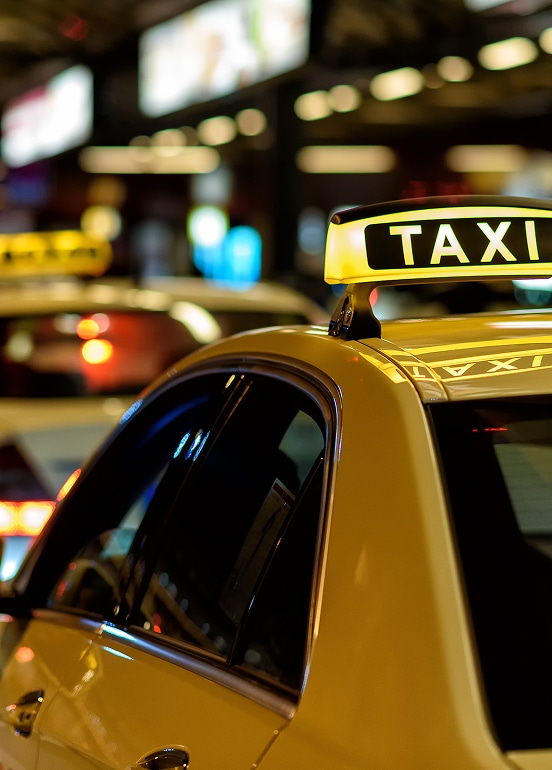 Taxi jaune avec enseigne lumineuse 'TAXI' la nuit en ville. Lumières urbaines floues en arrière-plan.
